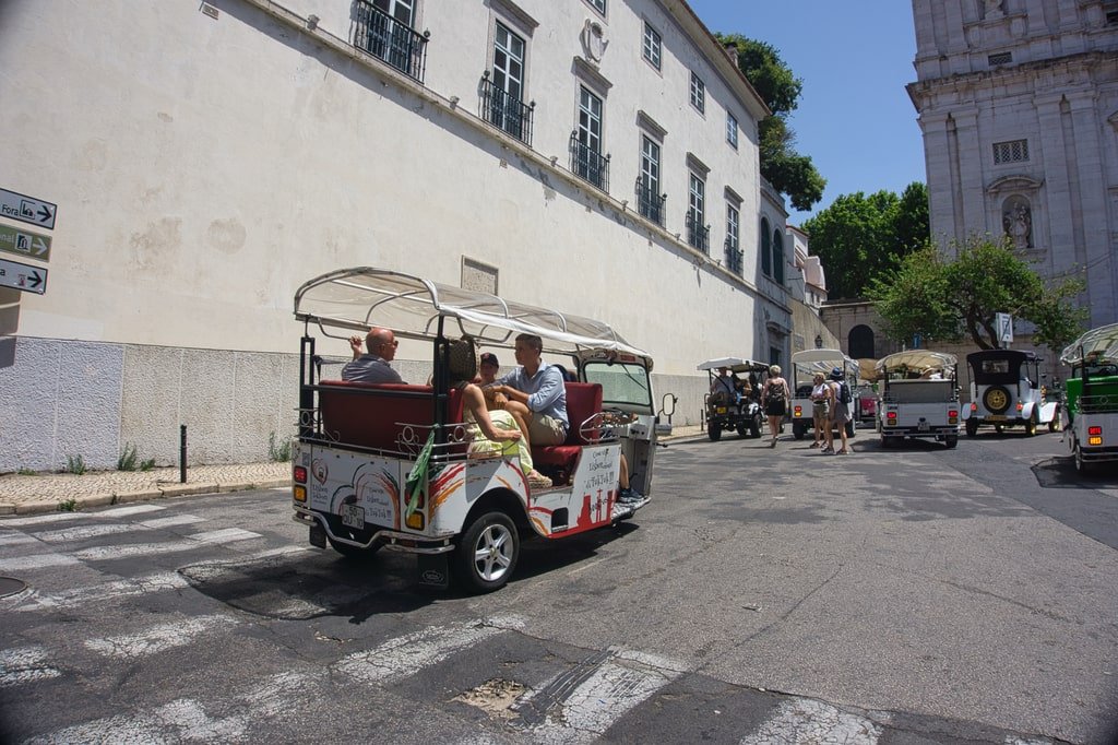 A white tuk tuk moves through the streets of Lisbon.