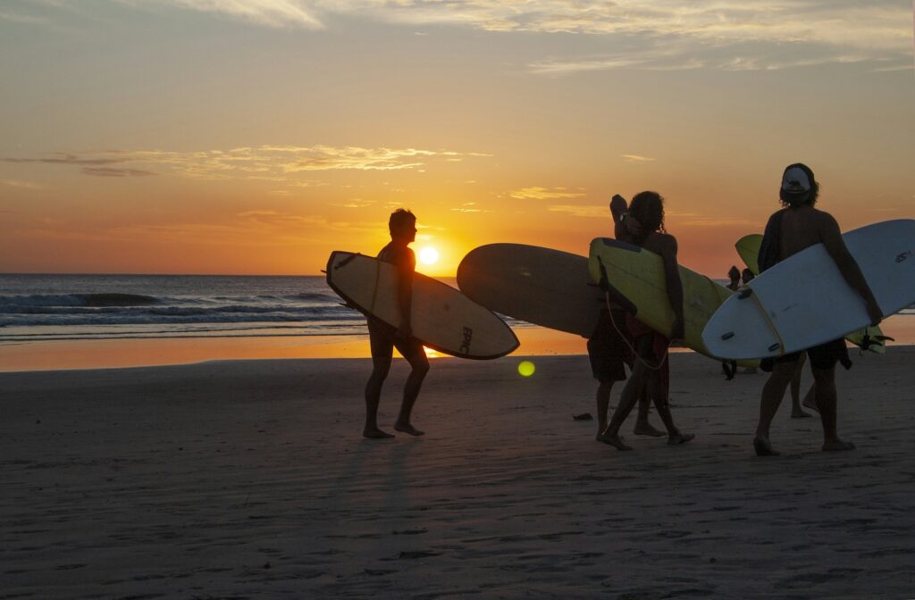 2 men holding surfboard walking on beach during sunset